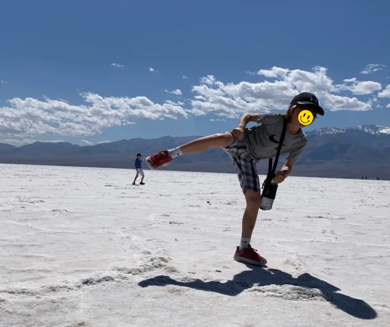 デスバレー国立公園の塩湖「バッドウォーターベイシン」の遠近法を利用して男の子が小さな男の子を蹴飛ばすような面白い写真。