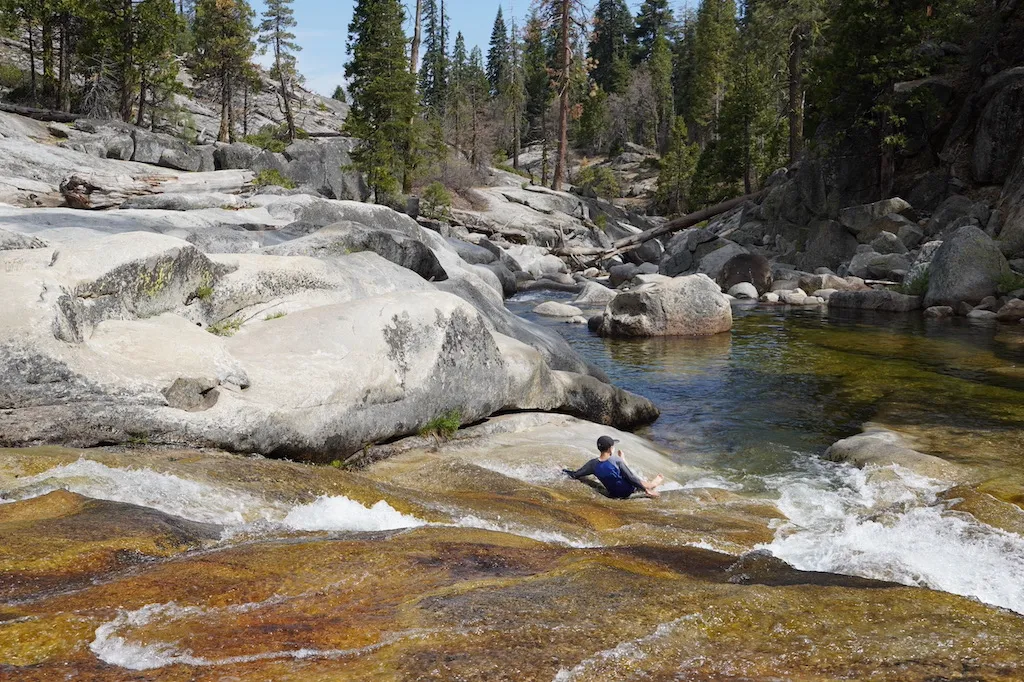 A boy is sliding a natural slide at a creek.