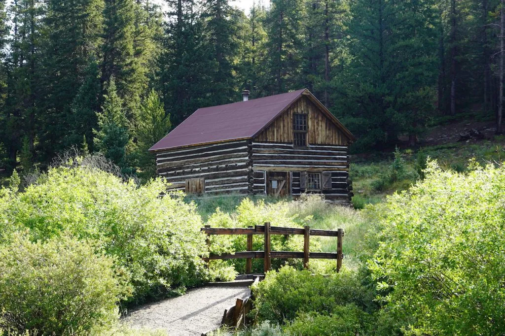 Old wooden cabin surrounded by bushes and trees at Roberts Cabin in Colorado.