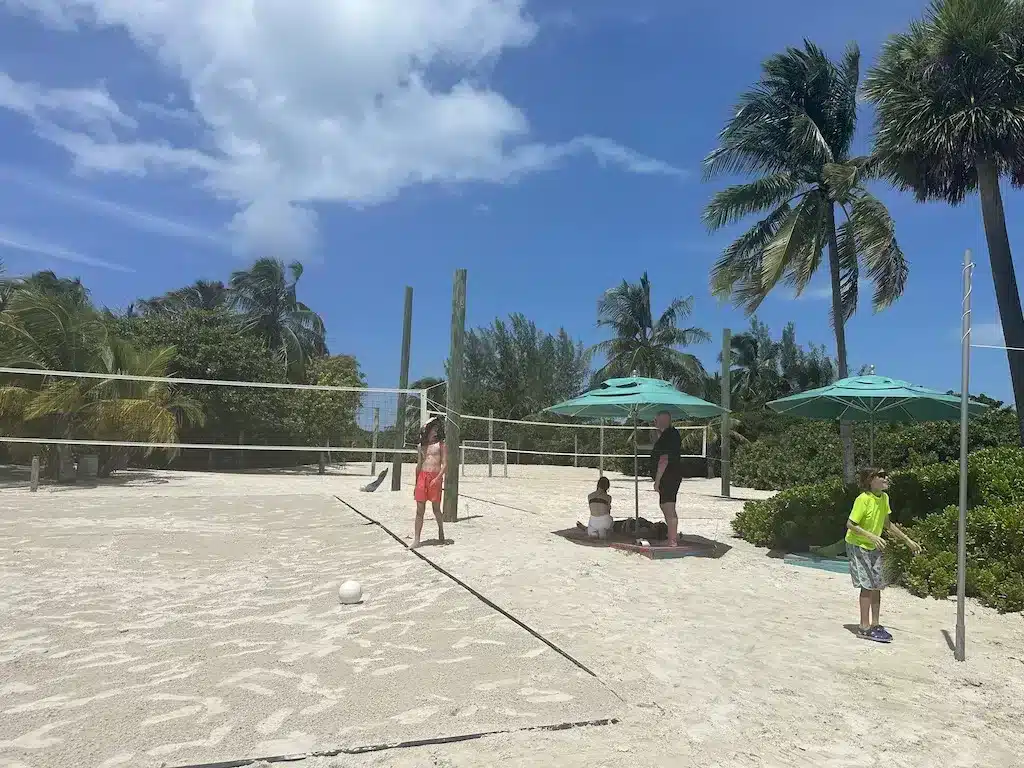 Children playing beach volleyball and tetherball on a sandy cout.