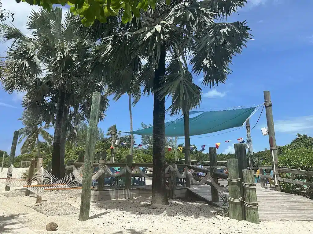 A hammock is strung between palm trees, and in the background, children are chatting and laughing on Castaway Cay.