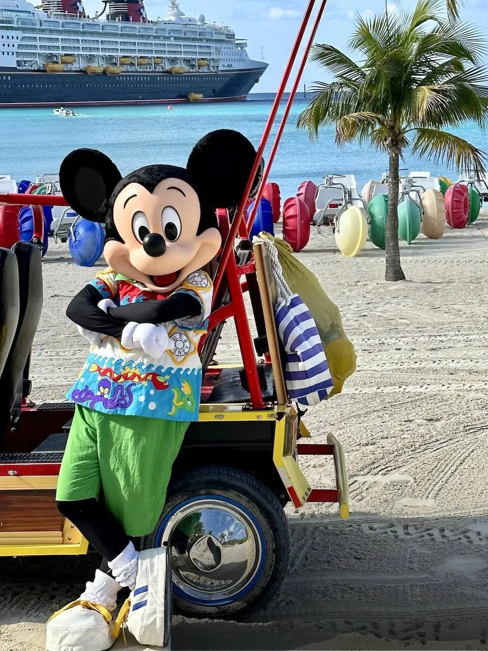 Mickey Mouse wearing a tropical shirt, leaning casually toward a golf cart at Castaway Cay.