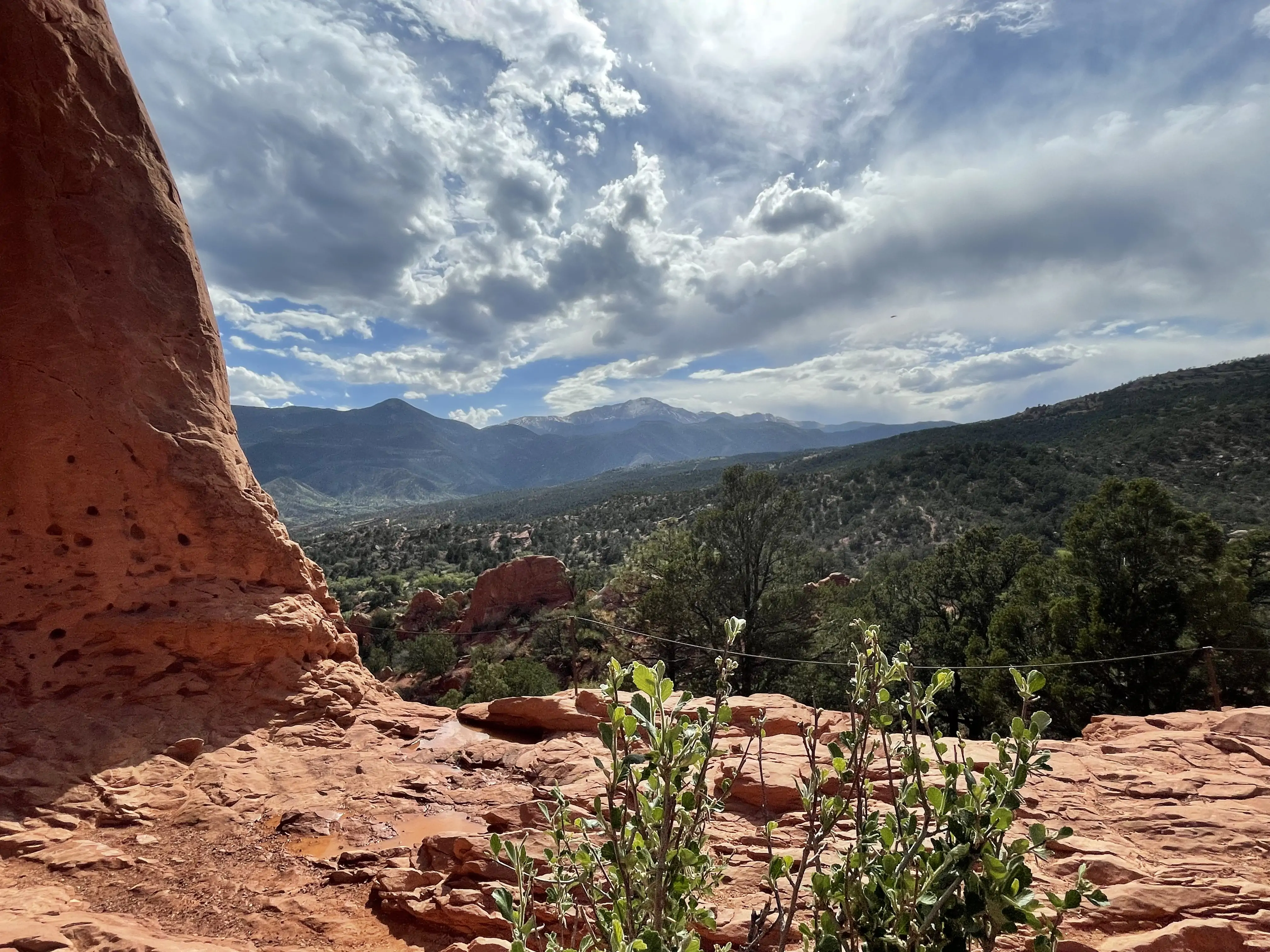 example of where to go near denver with this picture from Garden of the Gods in Colorado with the red rocks over looking a cliff and other mountains and a cloudy blue sky