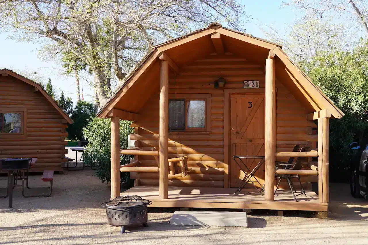 木に囲まれた静かなキャンプ場にある、ポーチと焚き火台付きのKOAキャンプキャビン