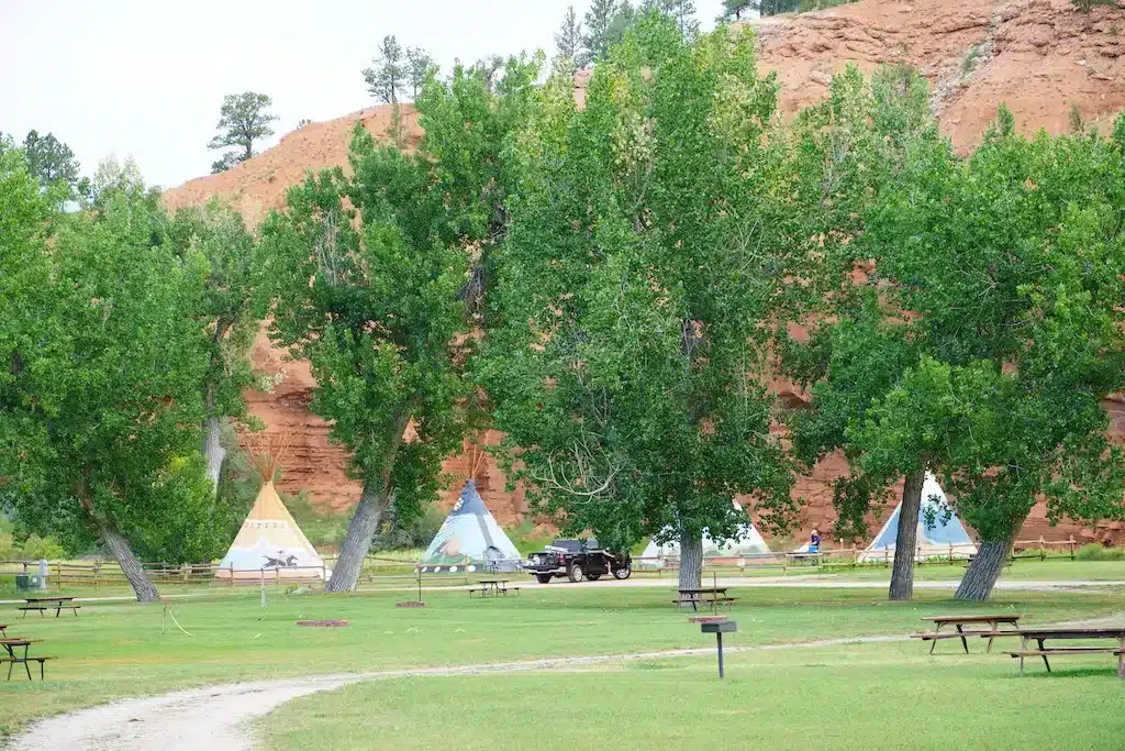 緑の木々と赤い岩山に囲まれたKOAキャンプ場に並ぶカラフルなティーピー。自然の中で楽しめるユニークなアメリカのグランピング体験