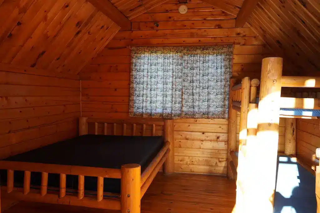 木の温もりを感じるKOAキャビンの室内。ダブルベッドと二段ベッドが設置されたシンプルで温かみのある空間