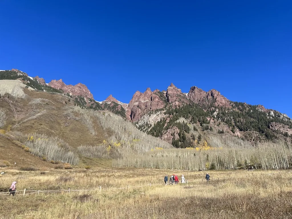 People are walking on the trail underneath the red mountains.