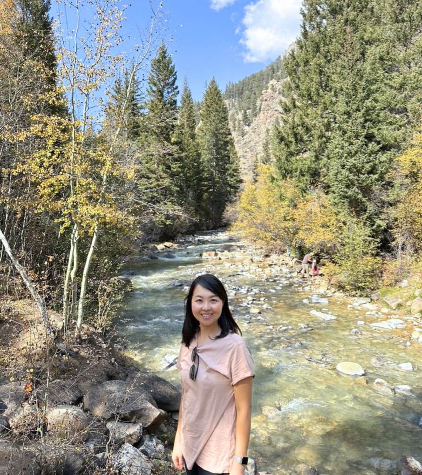 Tomo Colorado standing next to creek with blue skies and pine trees in Colorado