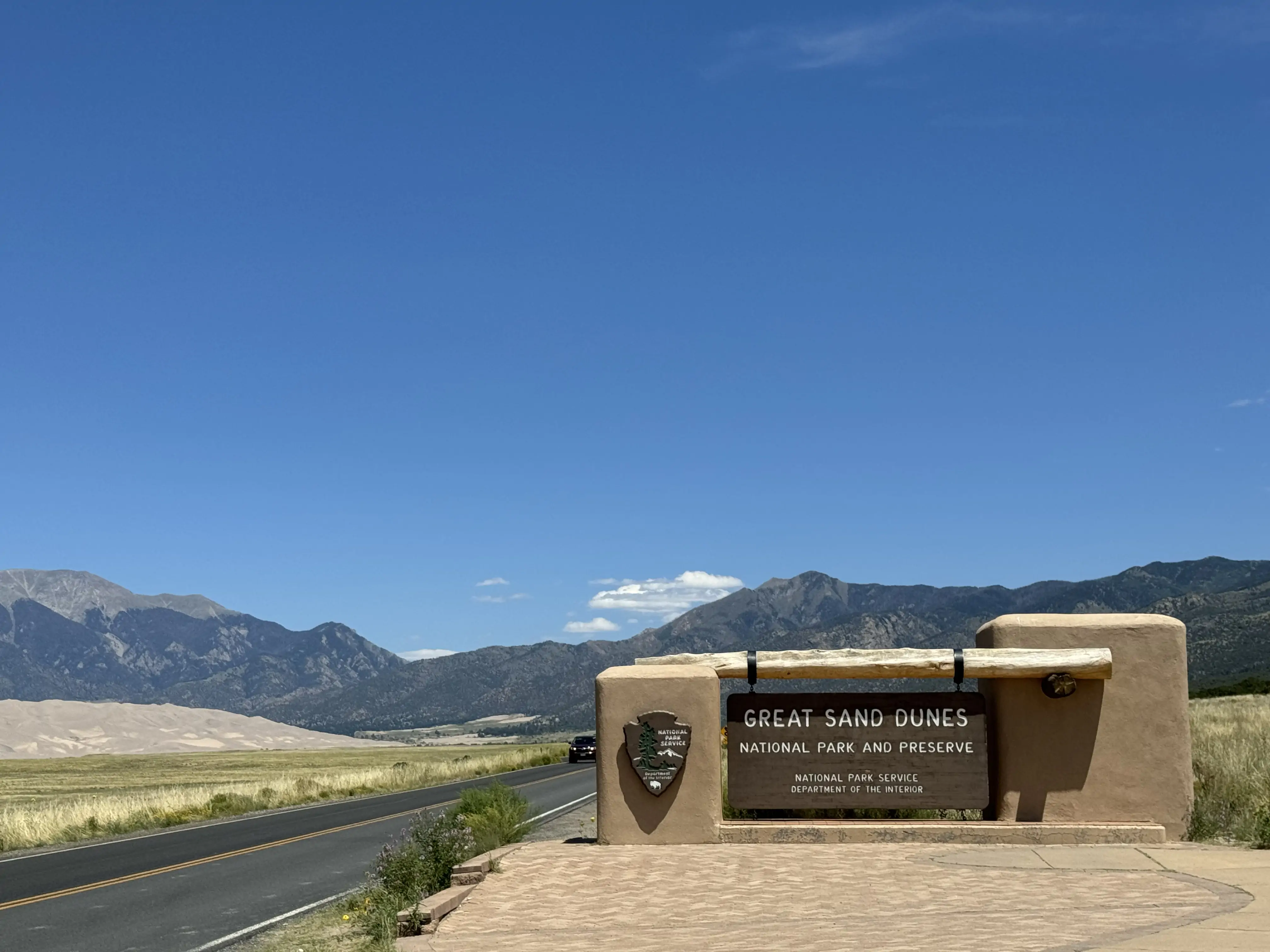 The sign of Great Sand Dunes with the expansive sand dune landscape in the background.