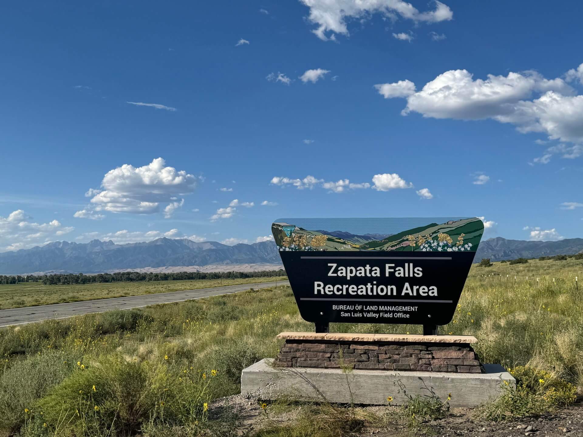 Bureau of Land Management sign of Zapata Falls Recreational Area with background of beautiful Great Sand Dunes National Park.