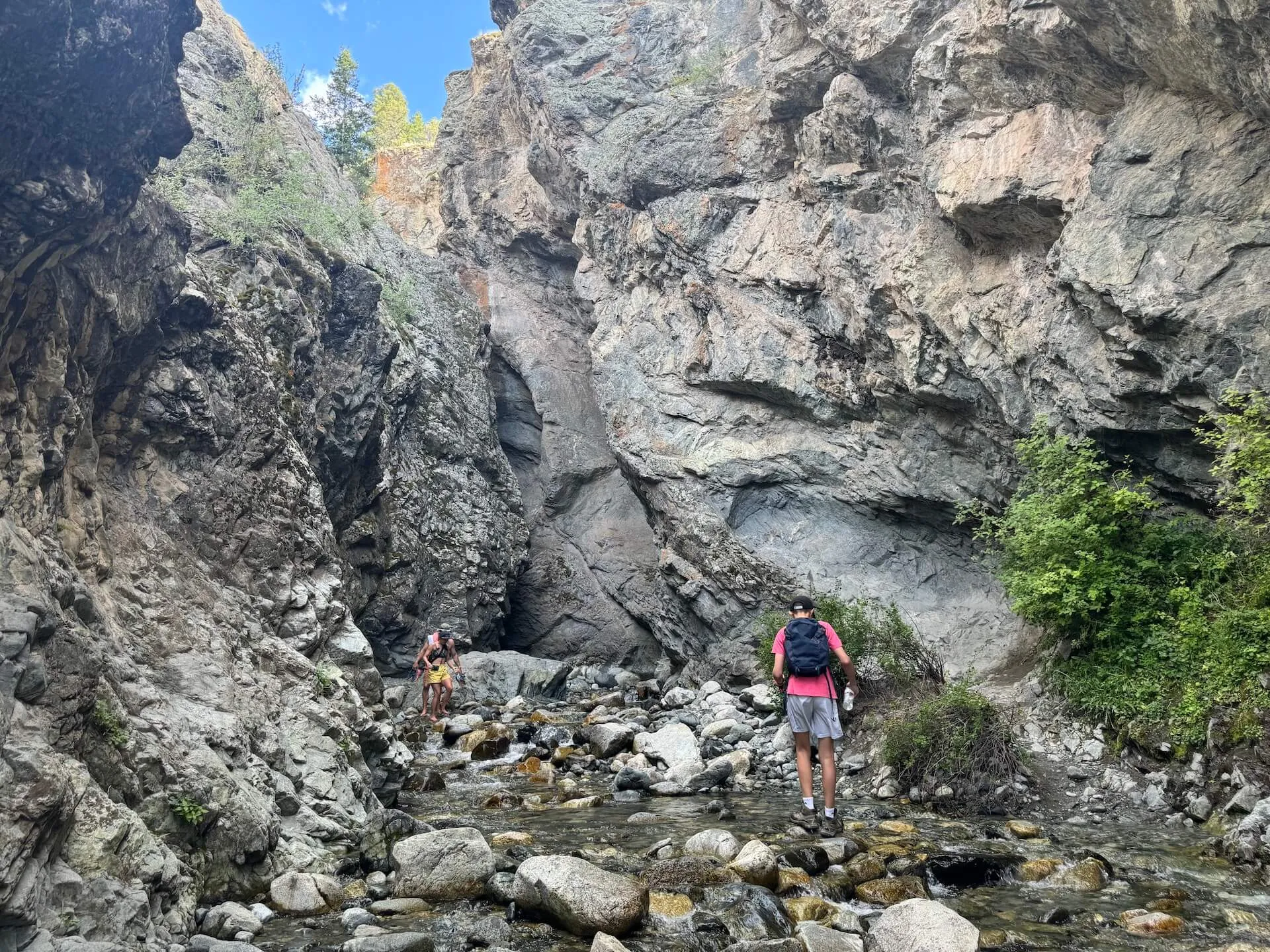 Hikers exploring Zapata Falls in Colorado, walking along a rocky creek surrounded by towering canyon walls near Great Sand Dunes National Park.