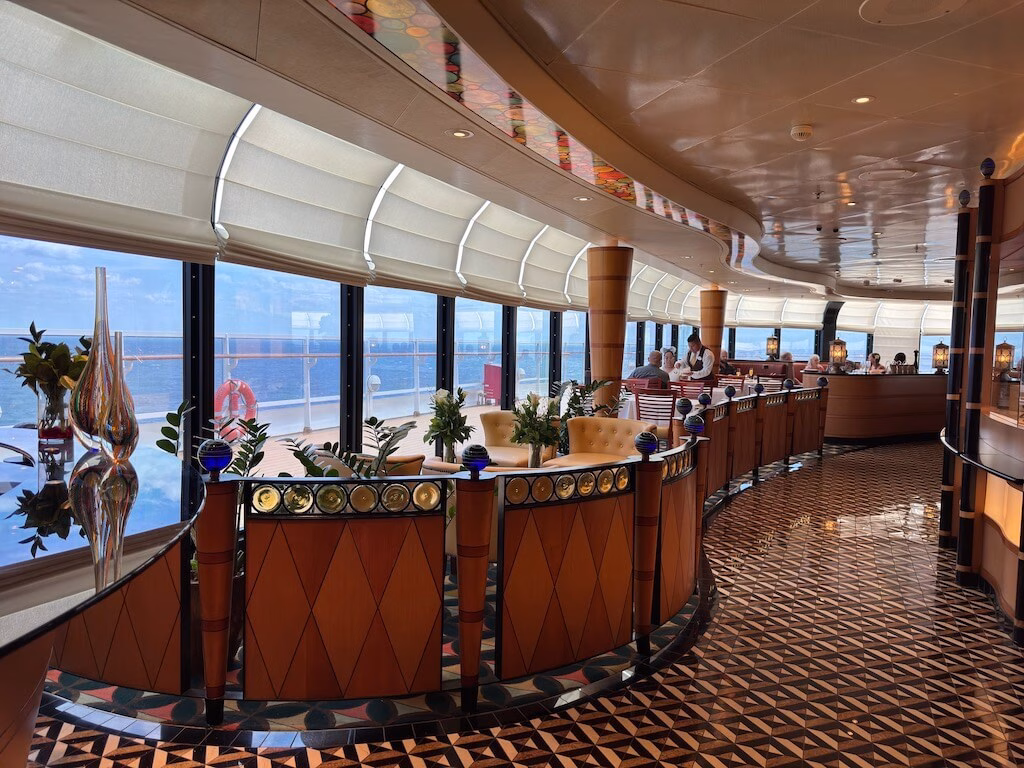 Interior of Palo, the adults-only Italian restaurant on the Disney Magic cruise ship, featuring elegant decor with warm lighting, wooden floors, and large windows showcasing ocean views. Tables are set with fine linens and polished silverware, creating a sophisticated dining atmosphere.