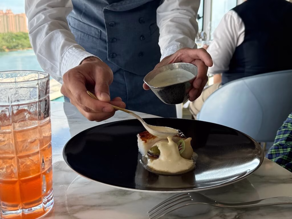 The server at Enchanté restaurant on the Disney Wish who pours cream over the fish dish.