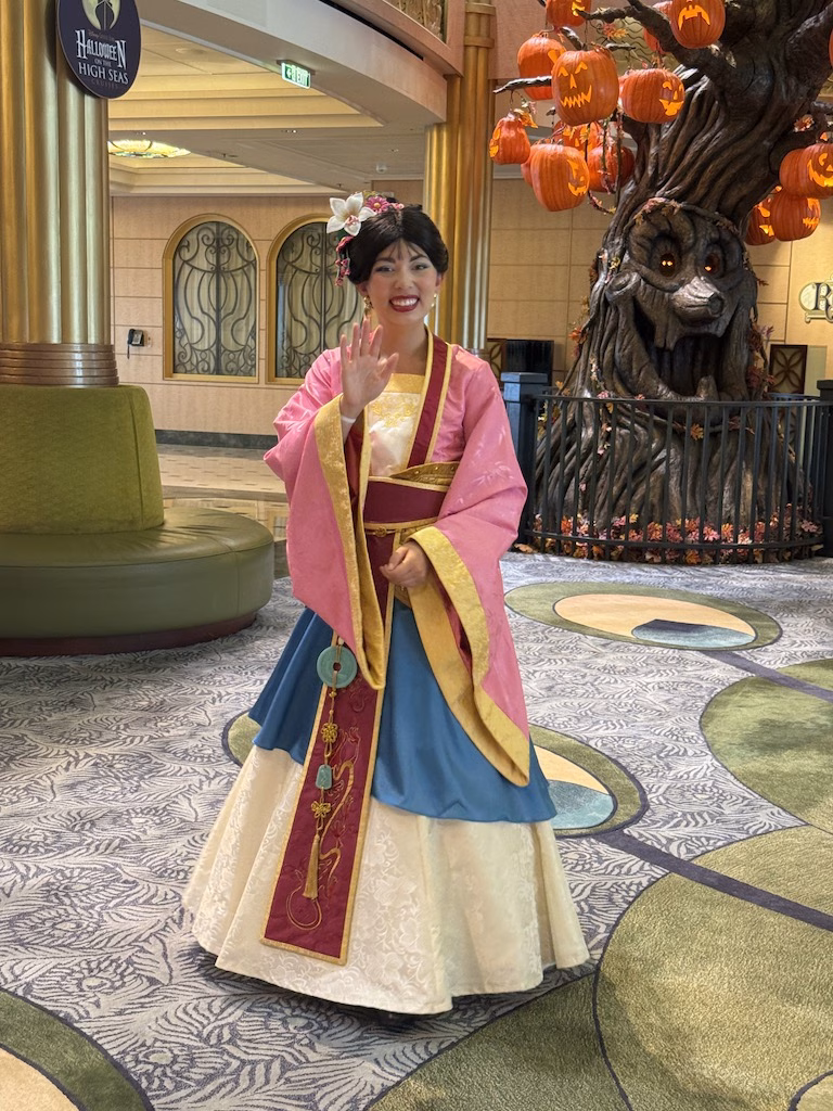 Mulan, the Disney Princess, cheerfully waving in the lobby of the Disney Fantasy.