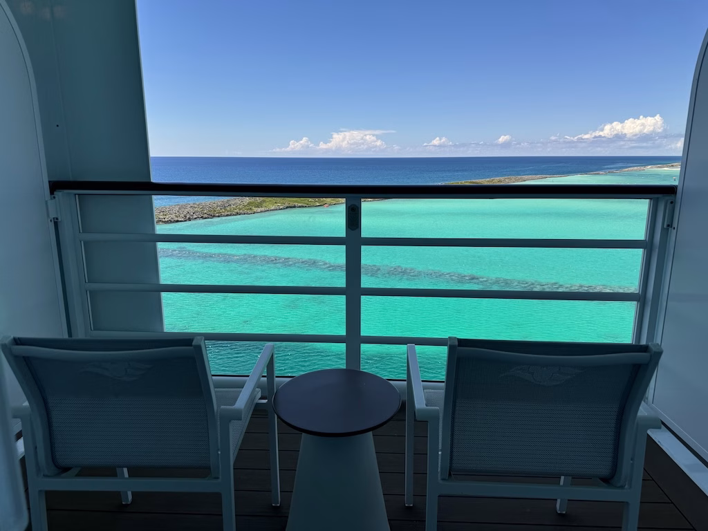 A veranda stateroom on the Disney Wish cruise ship, with the stunning emerald-blue waters of Castaway Cay in the background.