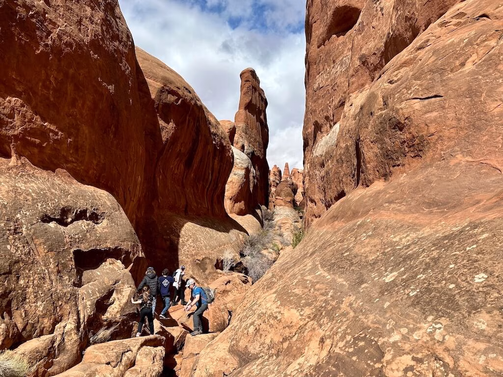 Hikers exploring a narrow sandstone canyon inside the Fiery Furnace Trail at Arches National Park, one of the most adventurous and scenic hikes in Moab, Utah.