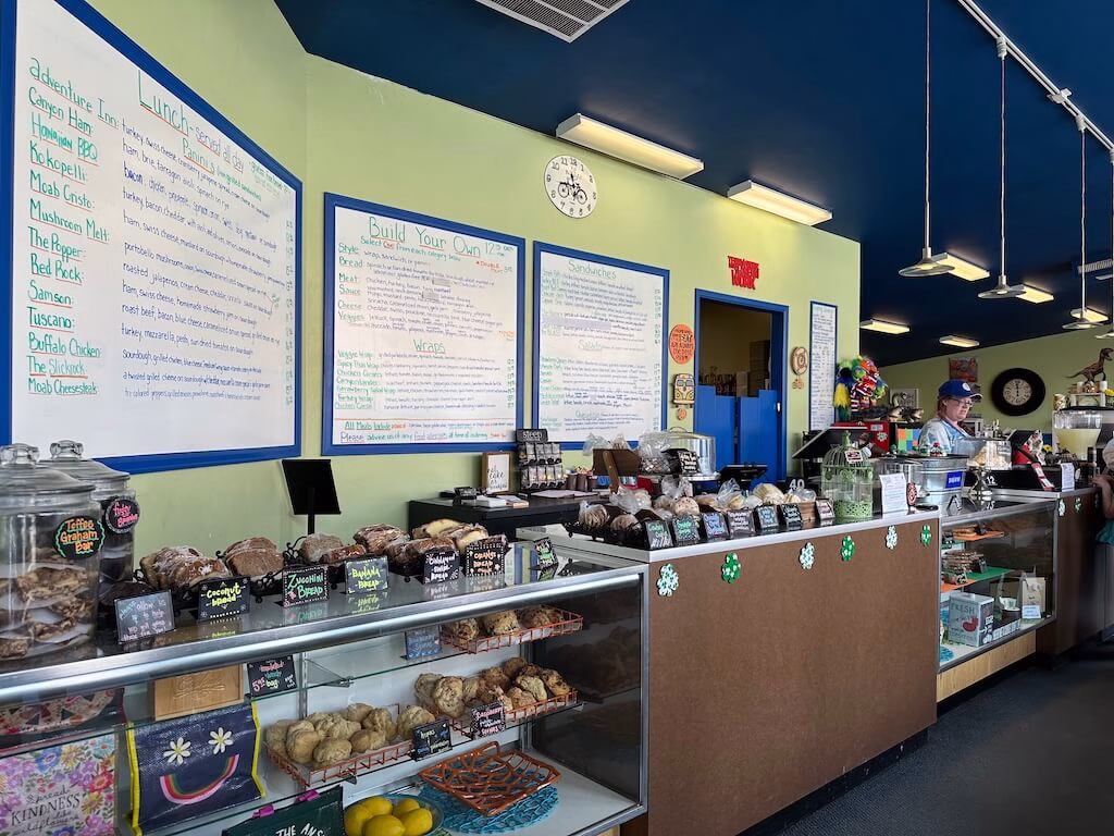 ユタ州モアブの人気店「Sweet Cravings Bakery + Bistro」の店内。サンドウィッチや焼き菓子が並ぶショーケースと、大きな手書きメニューが壁に掲げられている。テイクアウトにも便利なローカルベーカリー＆ビストロ。