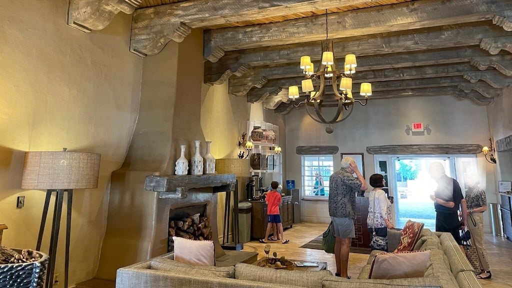 Hilton Santa Fe Lobby – Southwestern Elegance Near Meow Wolf and Top Santa Fe Attractions - Tomo Travel & Camping ニューメキシコ州サンタフェのヒルトン・サンタフェのロビー。南西部スタイルの木製梁、暖炉、くつろげるソファがあり、ミャオウルフや人気観光地巡りの拠点にぴったり