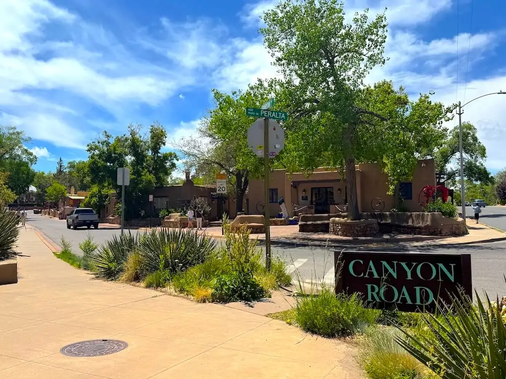 Canyon Road in Santa Fe, New Mexico, featuring adobe-style buildings, desert plants, and clear blue skies on a sunny day.