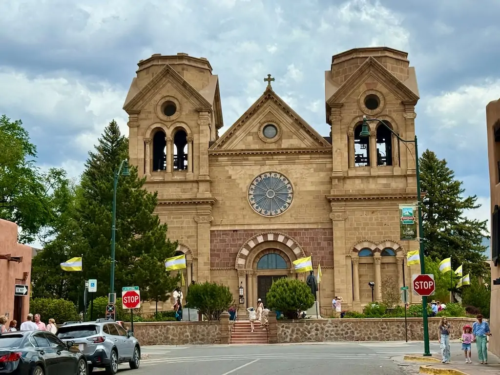 Front view of the Cathedral Basilica of St. Francis of Assisi in Santa Fe, New Mexico, with Romanesque architecture and waving flags—an iconic landmark for visitors exploring where to go in Santa Fe’s historic downtown.