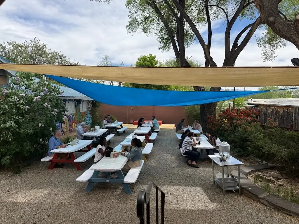 Picnic-style outdoor seating under shade cloth at Alys A La Cart food truck in Taos, New Mexico, with diners enjoying lunch.