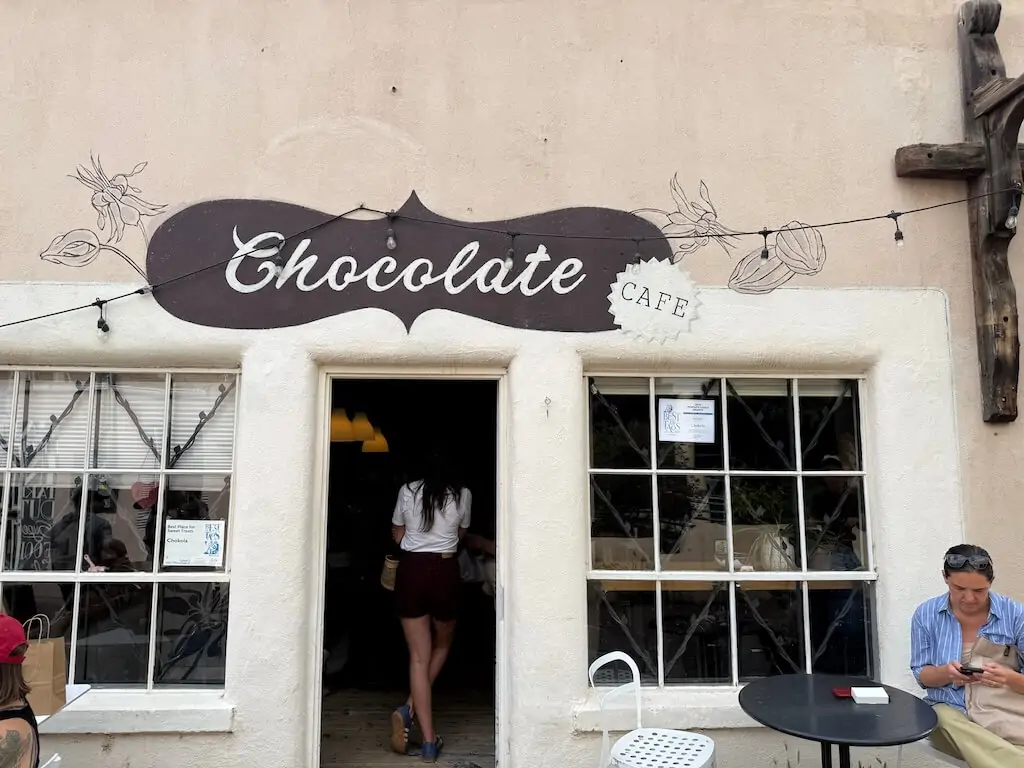 Front of Chokola Café in Taos, New Mexico, a small bean-to-bar chocolate shop with a hand-painted sign and seating outside.