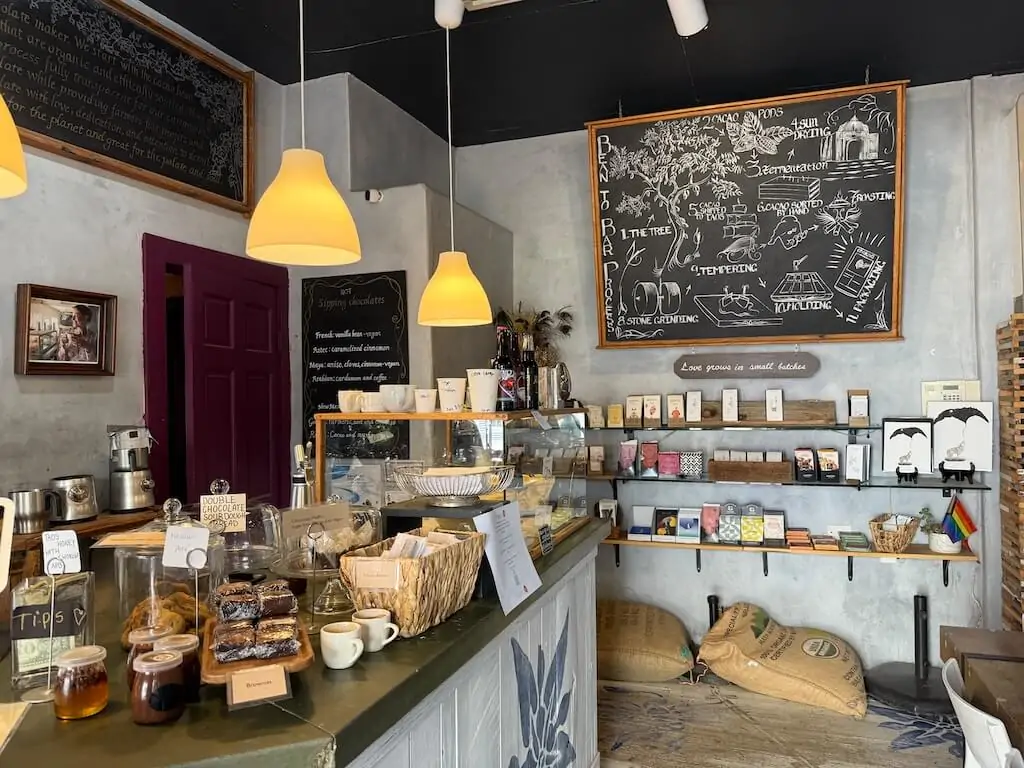 Interior view of Chokola bean-to-bar chocolate shop in Taos, New Mexico, showing baked goods, chocolate bars, and chalkboard menu.