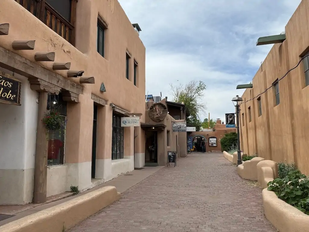 Narrow alleyway lined with adobe buildings and boutique shops in downtown Taos, New Mexico.