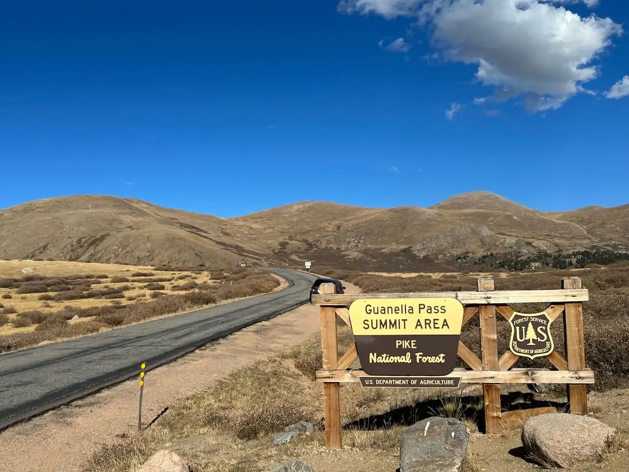 Guanella Pass Summit Area sign with open mountain landscape under a bright blue sky in Colorado.