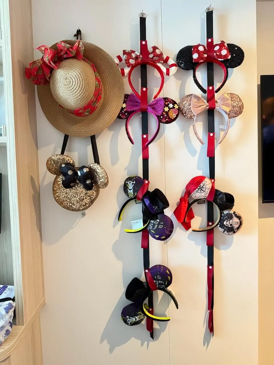 Disney Cruise stateroom wall with Minnie ear headbands and hats neatly organized using hanging straps and magnetic hooks