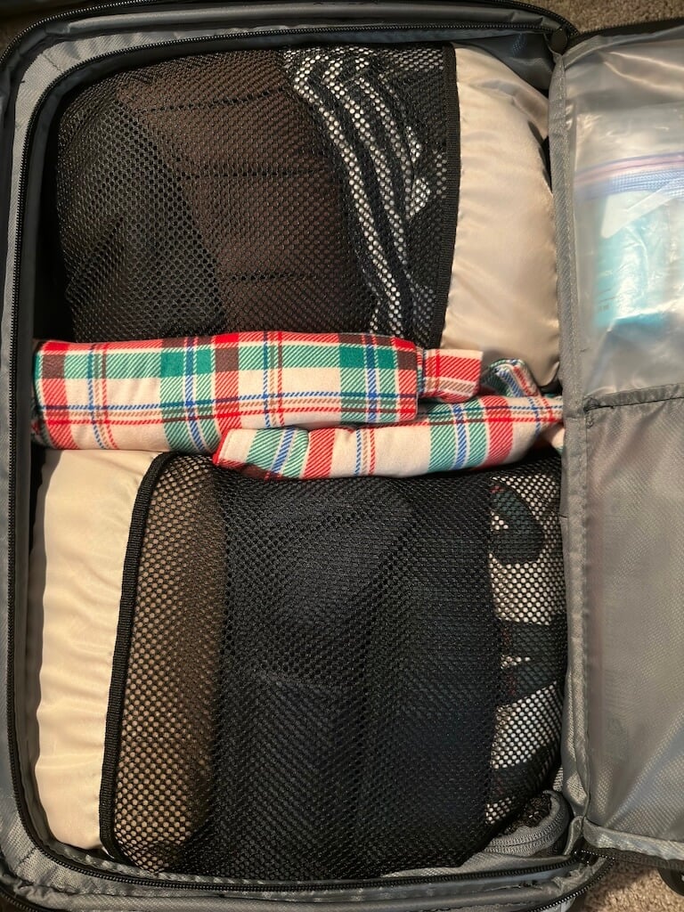 Suitcase packed with beige and black packing cubes keeping clothes neatly organized for a Disney Cruisec - Tomo Travel & Camping ディズニークルーズ旅行の荷造りに使うベージュと黒のパッキングキューブ。衣類をすっきり整理し、スーツケース内のスペースを有効活用。