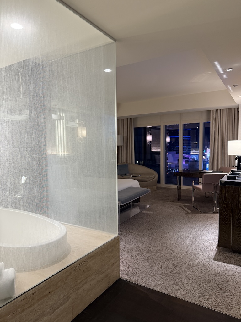 Waldorf Astoria Las Vegas Room with City View and Luxury Soaking Tub - Tomo Travel & Camping ウォルドルフ・アストリア・ラスベガスの広々とした客室。ガラス張りのバスタブ、キングベッド、夜のラスベガスの街並みが見えるシティビュー付き。