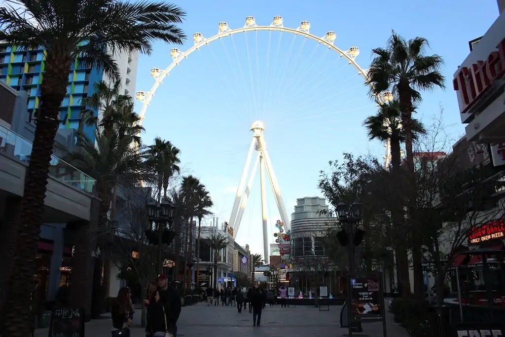 View of the High Roller Ferris wheel with palm trees and shops on the Las Vegas Strip