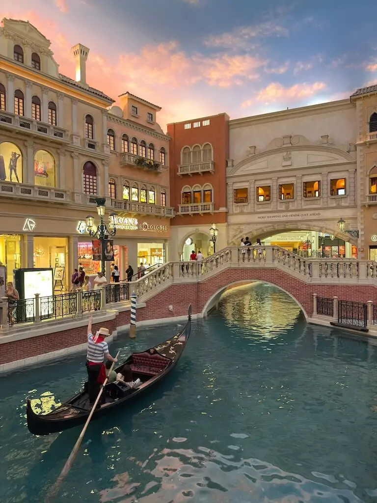 A gondolier rowing guests through the indoor canal at The Venetian Las Vegas under a pastel sunset sky