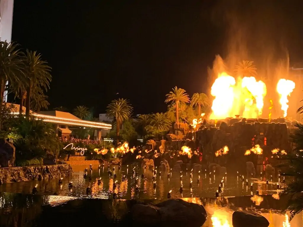 Fiery Mirage Volcano Show erupting at night in front of palm trees and the Mirage Hotel in Las Vegas