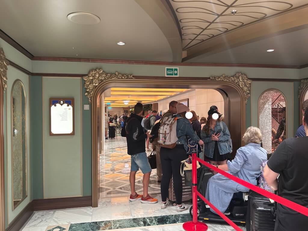 Guests waiting in line with luggage for Express Walk-Off disembarkation on a Disney Cruise ship