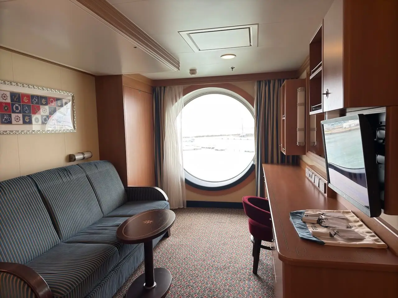 Disney Cruise oceanview stateroom with sofa seating area and large porthole window overlooking the ocean.