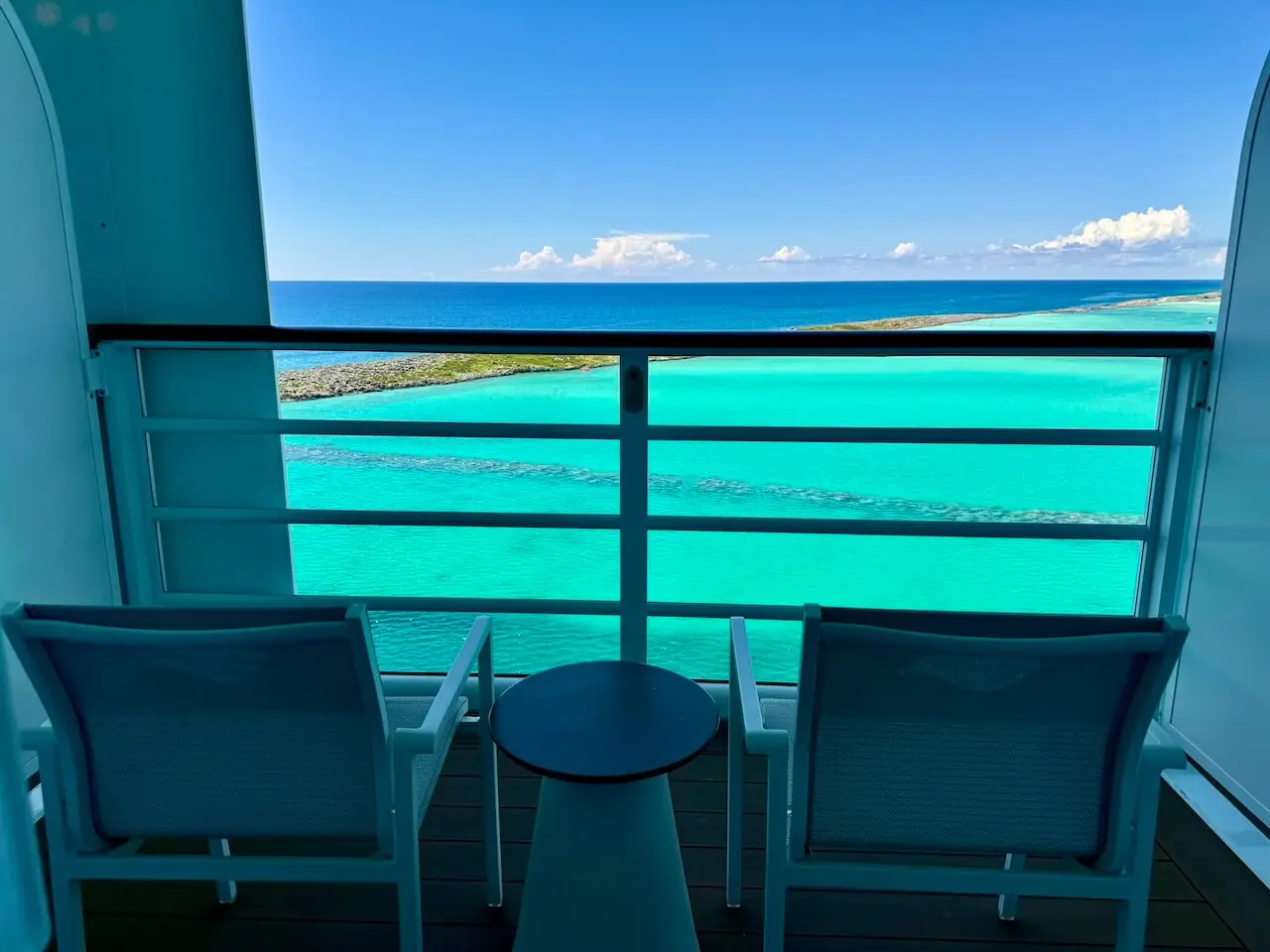 Disney Cruise verandah stateroom (booked with VGT) balcony with chairs overlooking turquoise ocean water.