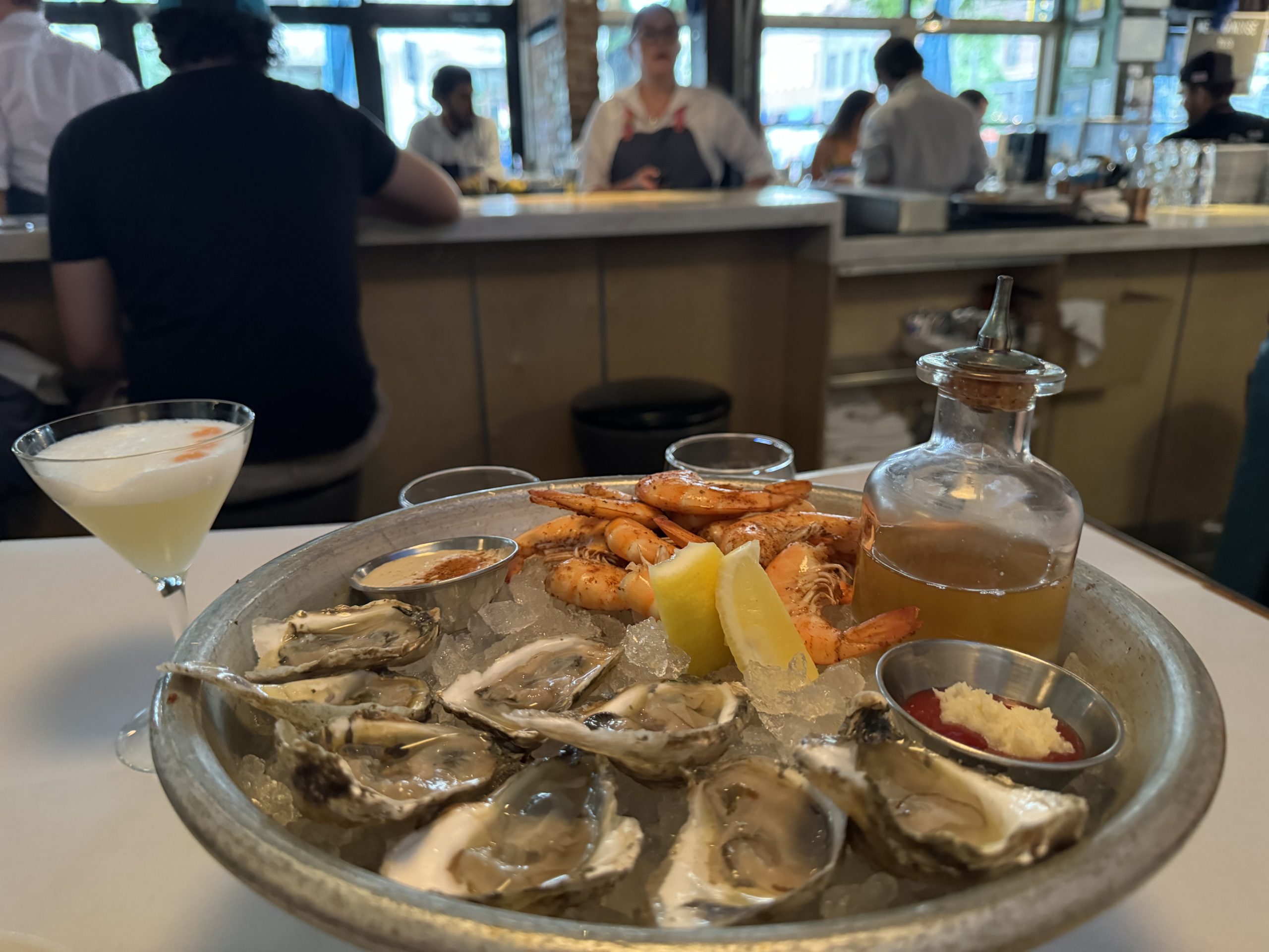 Denver Downtown Jax Fish House - Tomo Travel & Camping Seafood platter on ice with oysters, shrimp, lemon wedges, and dipping sauces on a metal tray at a restaurant in Denver.