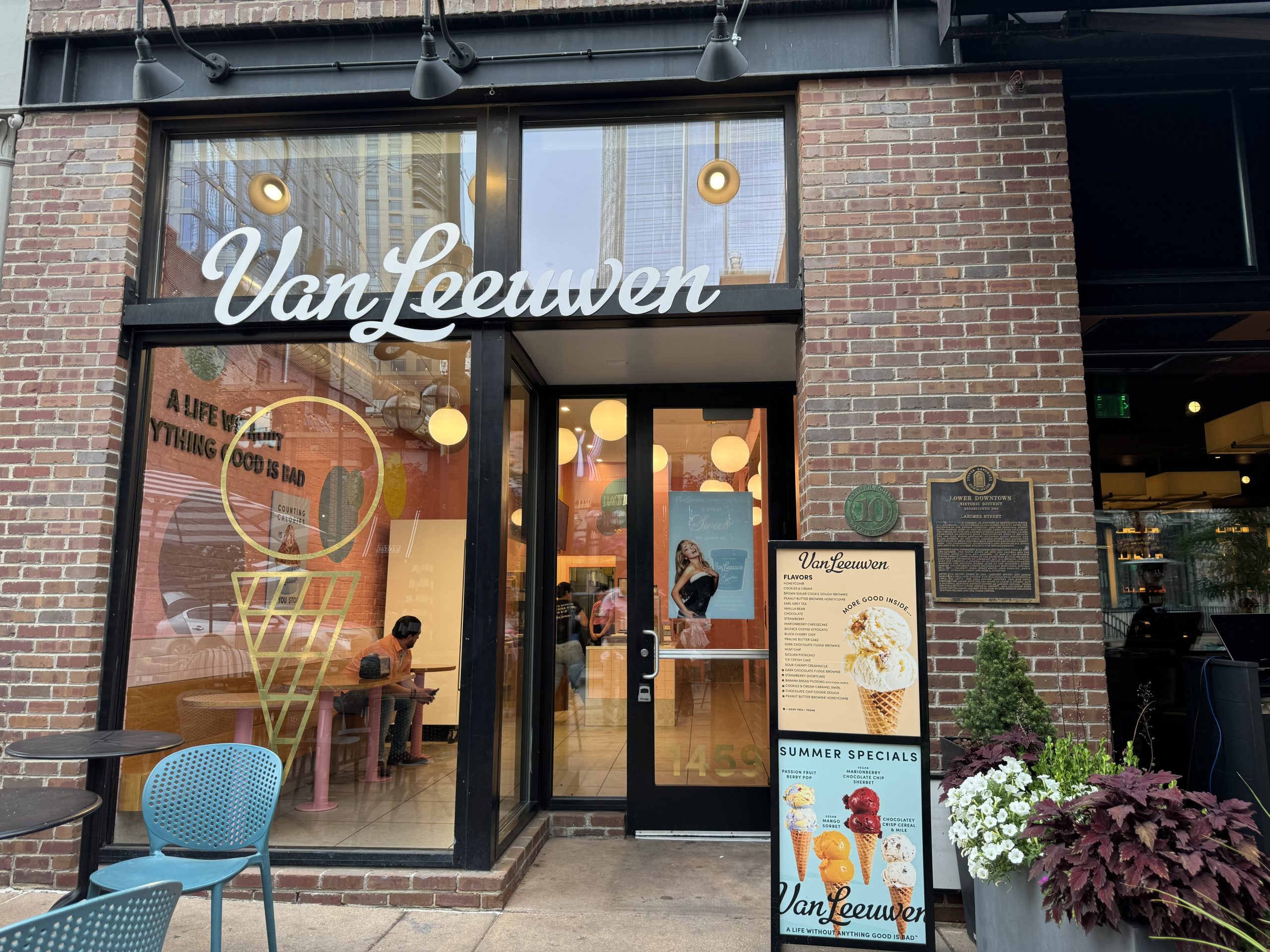 DenverDowntownVanLeeuwenIceCream - Tomo Travel & Camping Brick storefront of Van Leeuwen ice cream shop with large glass windows, sign, and a menu board outside in Denver.