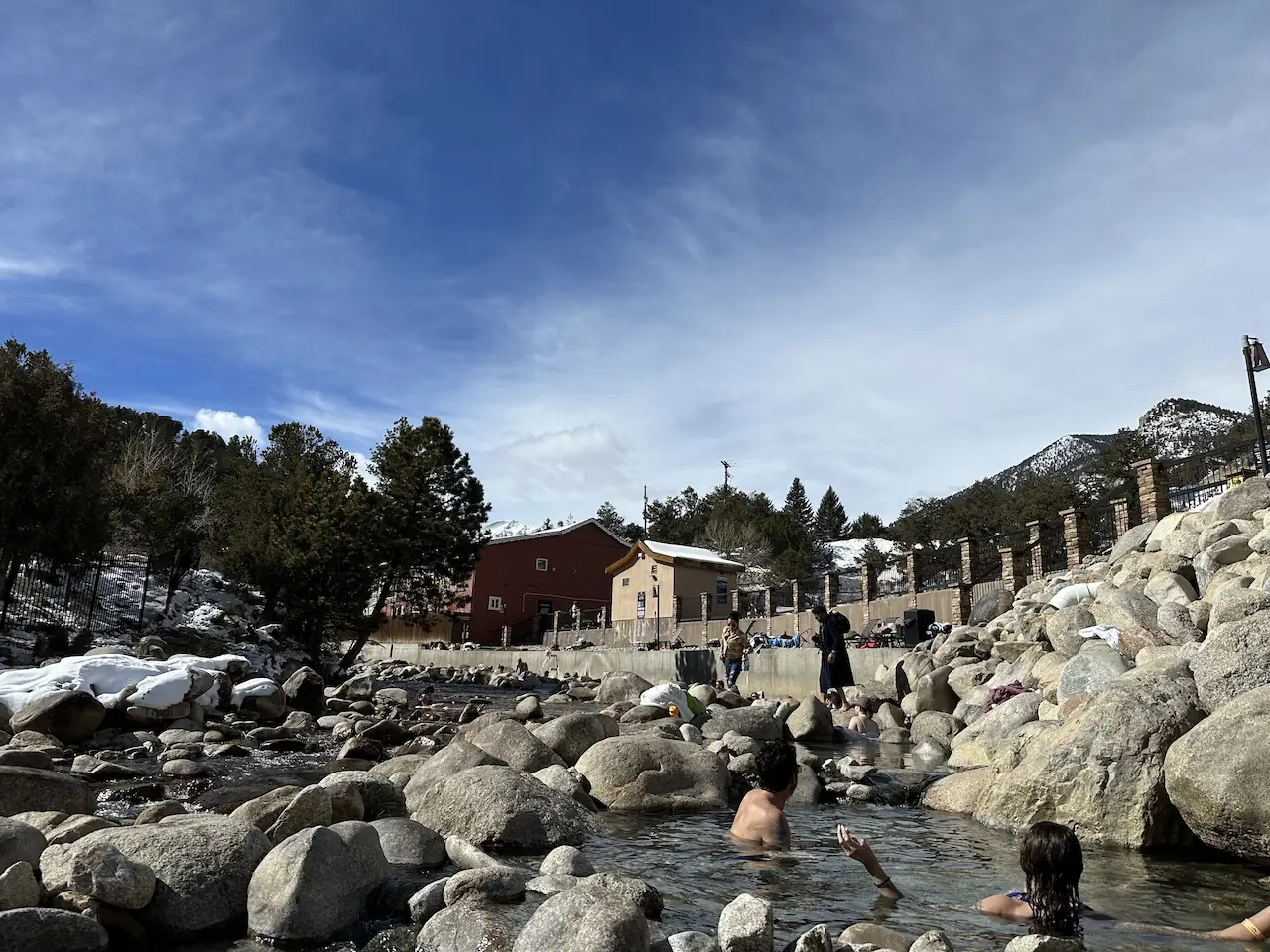 Travelers soaking in circular natural hot spring pools built into a rocky creek bed at Mount Princeton Hot Springs Resort in Colorado.