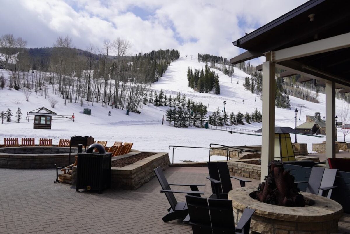 The outdoor patio at Park Hyatt Beaver Creek featuring stone fire pits and black Adirondack chairs overlooking the snowy ski slopes of Beaver Creek Mountain.