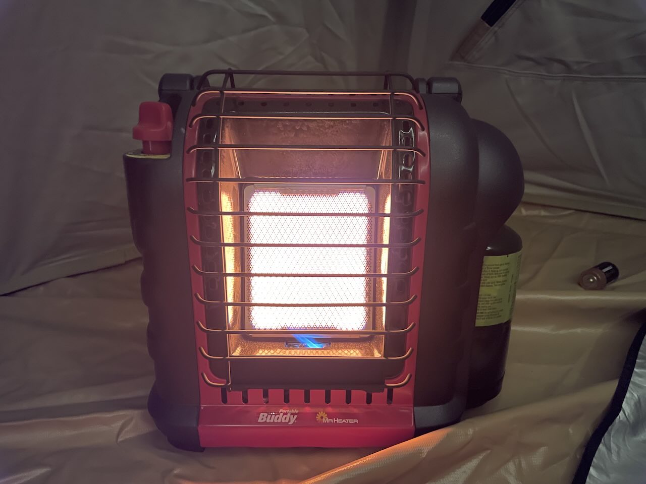 Mr. Heater Portable Buddy Propane Heater for Cold Night Tent Camping in National Parks - Tomo Travel & Camping Mr. Heater Portable Buddy propane heater glowing orange inside a tent at night during a cold weather family tent camping trip in a national park