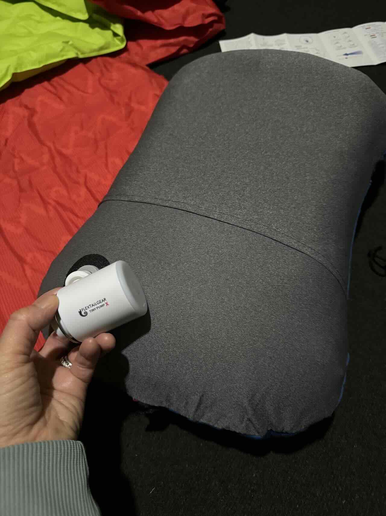Compact Air Pump for Inflating Sleeping Pads: Essential Tent Camping Gear for National Parks - Tomo Travel & Camping Hand holding a small white Flextailgear Tiny Pump X being used to inflate a gray sleeping pad inside a tent with colorful sleeping bags visible in the background