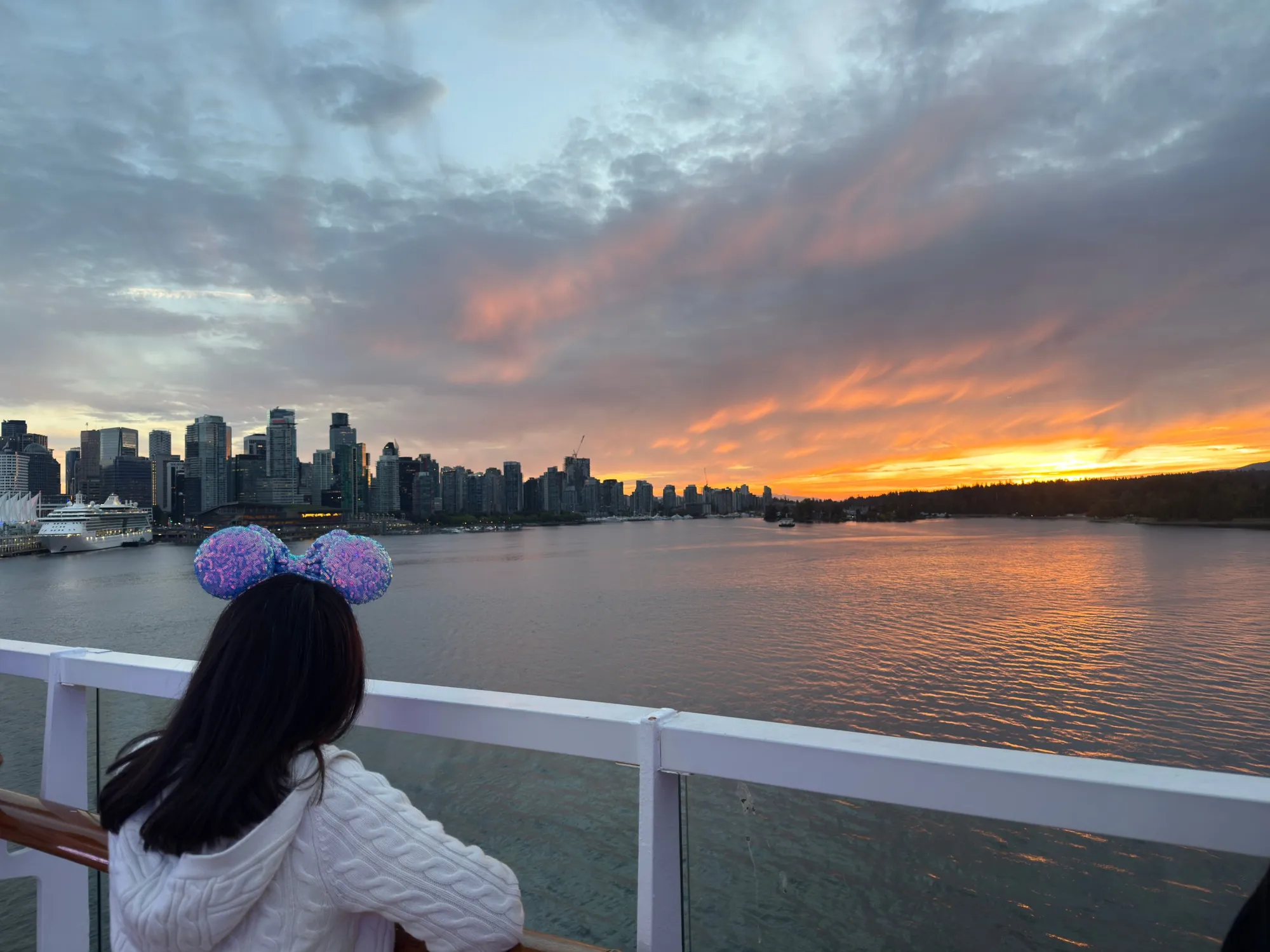 Tomo in a white cable knit sweater and Minnie ears watching the sunset over Vancouver from the deck of the Disney Wonder