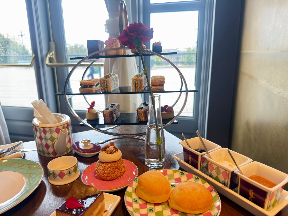 chateau-frontenac-afternoon-tea - Tomo Travel & Camping Tiered dessert stand with assorted pastries and a red rose in a vase on a tea table by a window.