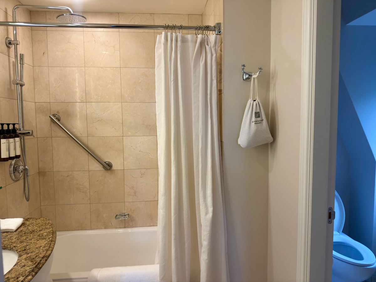 chateau-frontenac-bathroom - Tomo Travel & Camping Hotel bathroom with bathtub and shower curtain, beige tiled walls, and a granite counter with toiletries on the left.