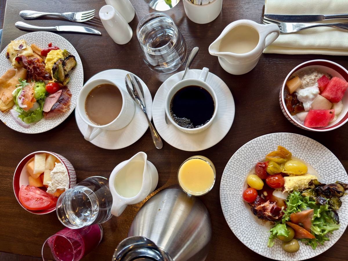 chateau-frontenac-breakfast-buffet - Tomo Travel & Camping Brunch spread on a wooden table: plates of salad, fruit, yogurt, coffee, and juice with utensils nearby
