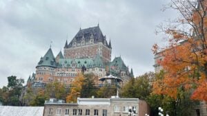 chateau-frontenac-featured-1200x675 - Tomo Travel & Camping Fairmont Le Château Frontenac hotel with green copper roofs atop a hill, autumn trees in the foreground under a cloudy sky, Canada flag visible