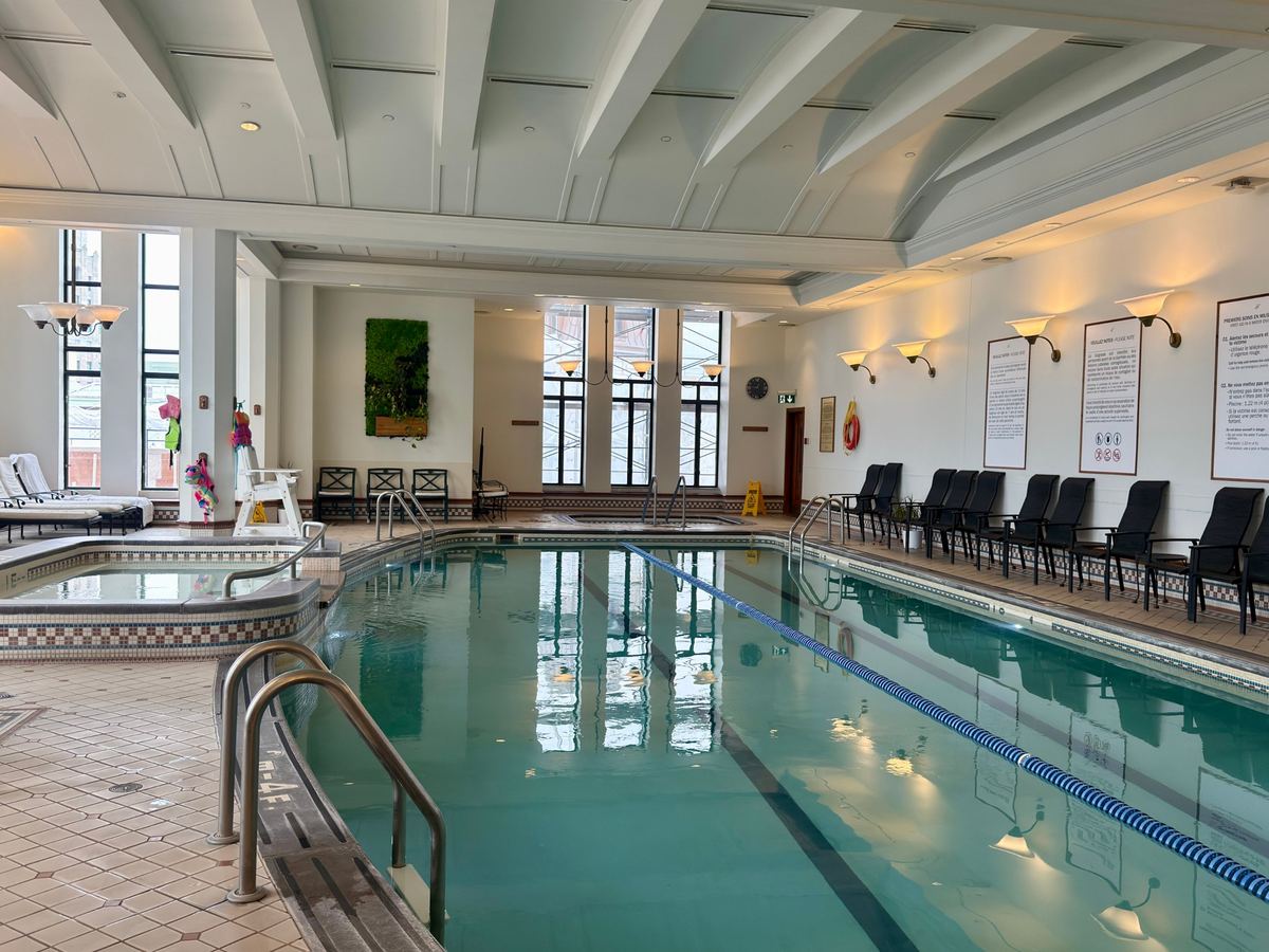 chateau-frontenac-indoor-pool - Tomo Travel & Camping Indoor pool area with lane ropes, lounge chairs along the wall, and large windows letting in natural light.